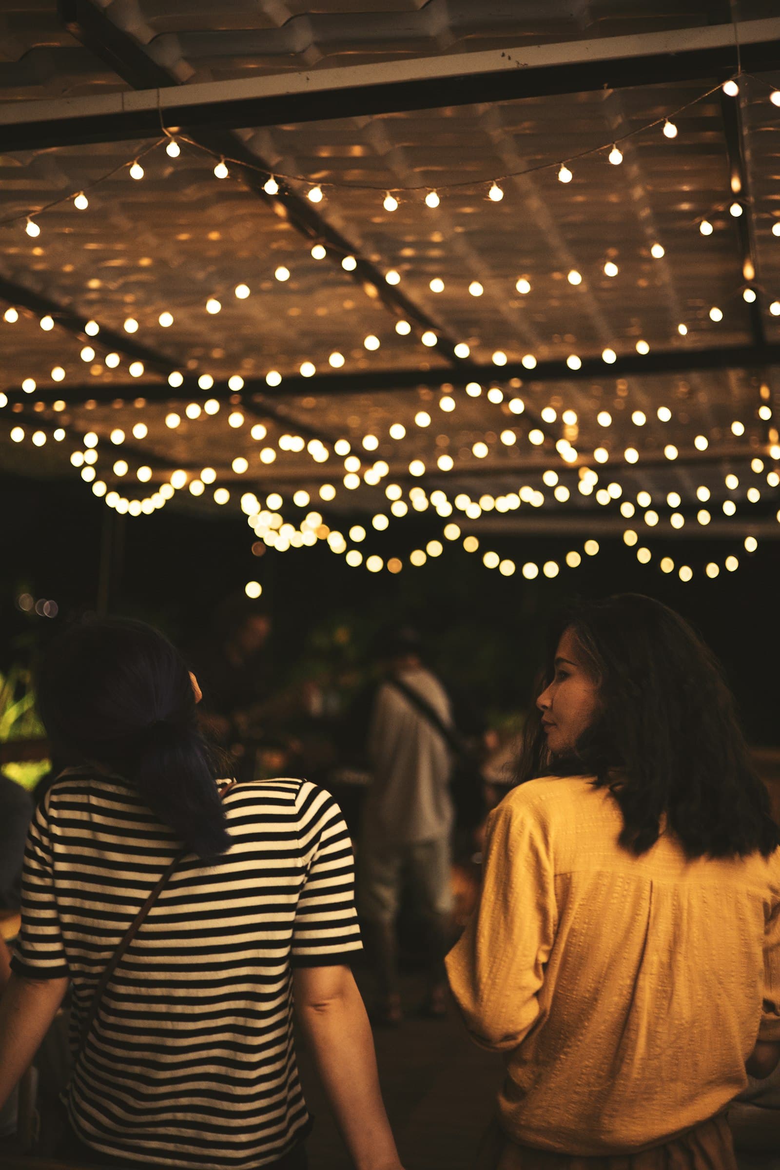 Two friends walking under string lights at night