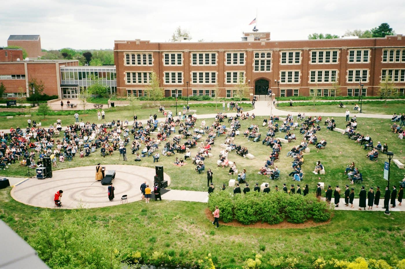 Students spread out across a sunny campus lawn in front of a brick building